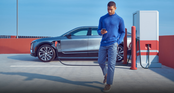  Side view of a GM vehicle EV charging at a public charging station as a person passes by.